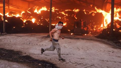 A young man runs next to a burning farm as a wildfire burns in central Greece