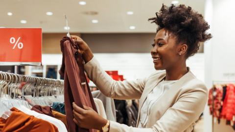 A woman in a white blazer shops in a clothing store