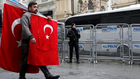 A man carrying Turkish flags walks past a Turkish armed riot policeman in front of the Dutch Consulate in Istanbul, Turkey, 13 March 2017.
