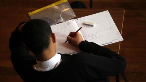 A student holds a pencil as they sit a maths exam