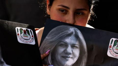A Palestinian holds up a photo of Shireen Abu Aqla as her body is carried to Al Jazeera's offices in Ramallah, in the occupied West Bank (11 May 2022)