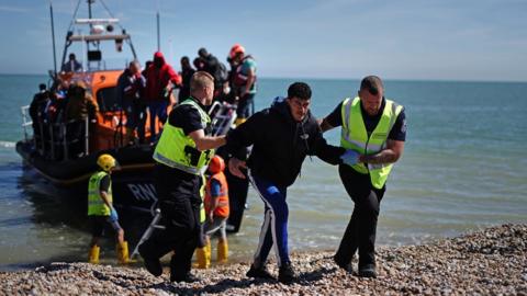 Migrants being helped off their boat and onto the shore by RNLI workers at Dungeness