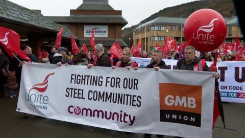 Protestors carry a banner saying union names and a close fighting for our steel communities