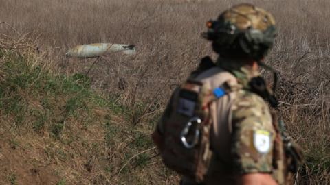 A Ukrainian soldier walks past an unexploded Russian bomb