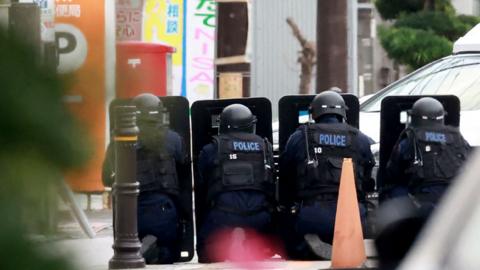 Police officers guard the area around a post office where a suspected gunman has taken an unknown number of people hostage in Warabi city, Saitama prefecture on 31 October 2023