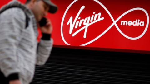 A man walks past a shop with Virgin Media branding