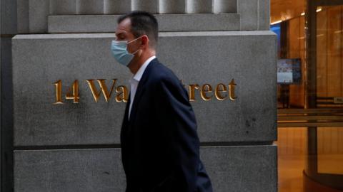 man wearing a protective face mask walks by 14 Wall Street, as the global outbreak of the coronavirus disease (COVID-19) continues, in the financial district of New York, U.S., November 19, 2020