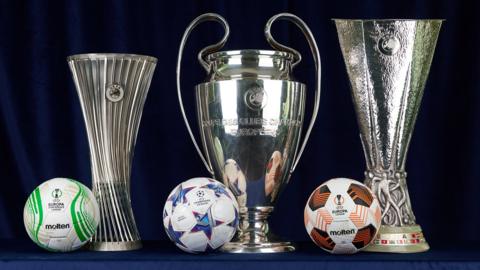 A photograph of the Europa Conference League, Champions League and Europa League trophies