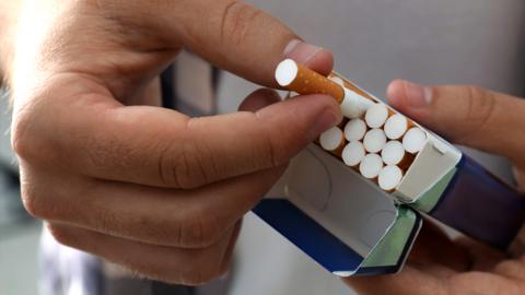 A man holds an open packet of cigarettes