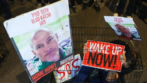 A man sits in a cage with portraits of hostage Elad Katzir during a demonstration in Tel Aviv in March