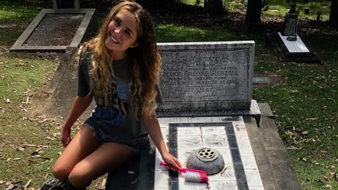 Girl sitting on grave with cleaning brush