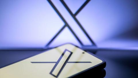 The X logo is being displayed on a smartphone, with the X app, formerly known as Twitter, and X visible in the background, in this photo illustration taken in Brussels, Belgium, on 5 January 2024.
