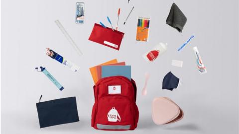 A red rucksack surrounded with school supplies, including stationery, water bottle and hygiene items, like a toothbrush.