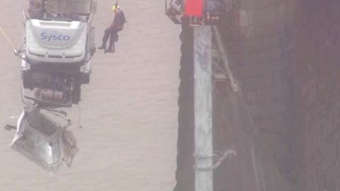 A rescue worker pulls a trapped person out of the cab of a lorry dangling over the edge of a bridge