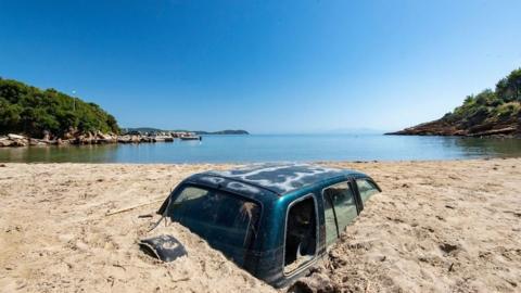 A car buried to the top of it doors on a sandy beach following a storm