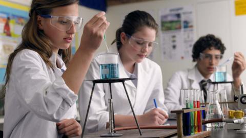 Three students in a science lab, dripping liquids into beakers.