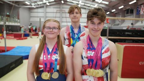 Grace, Simon and Jack standing in the gym. They are wearing their GB kits and have their necks.