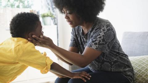 A woman is holding her son's face in her hands and he's got his hands on her knees