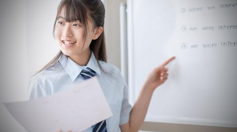 A female student stands at the front of a classroom.