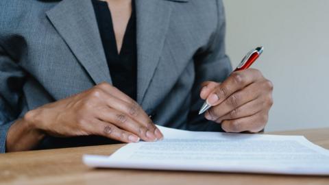 a woman in business attire reviewing/signing documents at desk