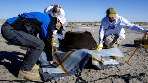 Lockheed Martin Mission Operations Assurance Lead Graham Miller, Lockheed Martin Recovery Specialist Michael Kaye, and Lockheed Martin Recovery Specialist Levi Hanish prepare the sample return capsule from NASA's OSIRIS-REx mission for transport shortly after the capsule landed at the Department of Defense's Utah Test and Training Range, on 24 September 2023 at the Department of Defense's Utah Test and Training Range in Dugway, Utah, US