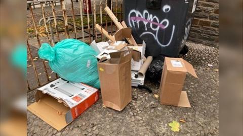 Piles of rubbish by a black bin