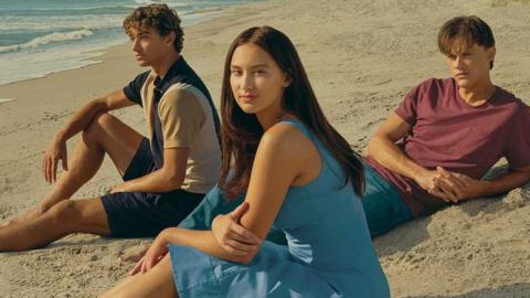 Three teenagers sit on a beach