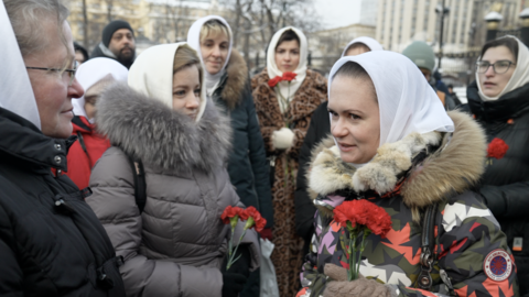 Group of Russian women stand around holding red flowers