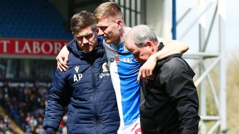 Blackburn defender Scott Warton is helped off the pitch by medical staff