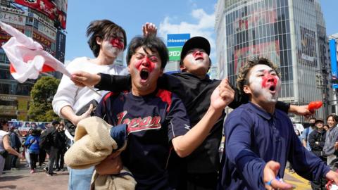 Exuberant young male fans with their faces painted red and white react to the winning pitch in Tokyo