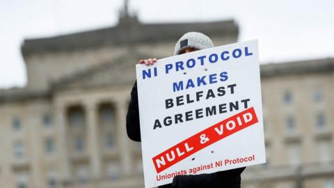 A loyalist protester at Stormont holds a sign that reads: NI Protocol makes Belfast Agreement null and void - unionists against NI Protocol