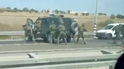 Man hides inside the car as soldiers run on road in Israel
