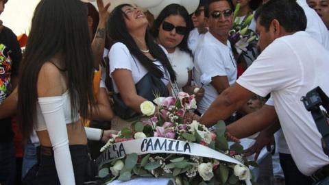 Mourners dressed in white by a coffin