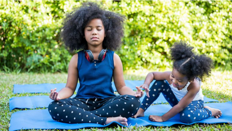 Two children meditate on a mat