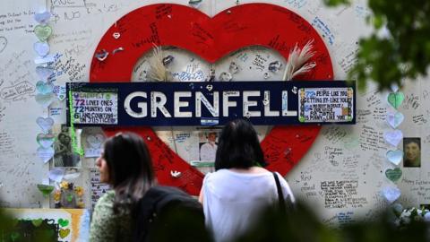 People stand in front of tributes on the Grenfell wall in London, Britain