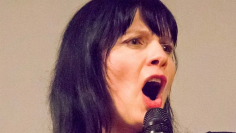 Comedian Lizzy Lenco on stage talking into a microphone