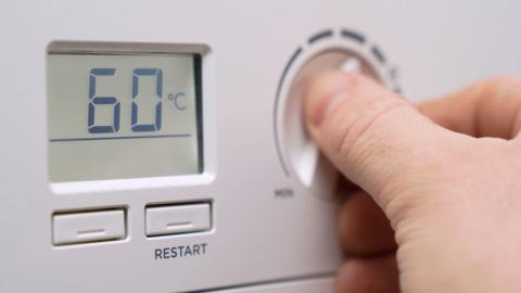 Person turning down temperature on gas boiler