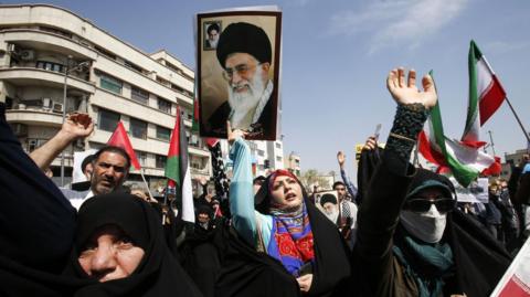 An Iranian woman (C) holds up a portrait of the Iranian supreme leader Ayatollah Ali Khamenei as others wave Iranian and Palestinian flags during an anti-Israel rally in Tehran