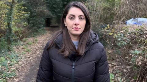 Reporter Maria Zacarro stood on a footpath wearing a black coat