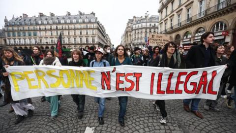 People holding a banner that reads 'No one is illegal' take part in a rally against the government's new immigration law, at Place du Louvre in Paris, France, 25 January 2024