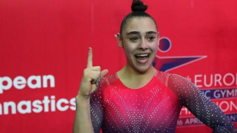 Jessica Gadirova makes the number one sign with her finger after winning gold