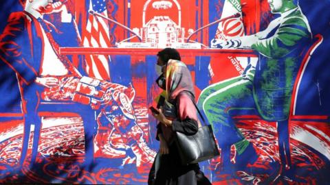 A couple, wearing protective masks amid the COVID-19 pandemic, walks past a mural painted on the outer walls of the former US embassy in the Iranian capital Tehran