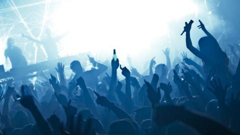 Nightclub disco crowd with arms and hands in air under blue lighting with performers on stage