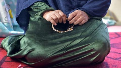 An Afghan woman sits while holding prayer beads