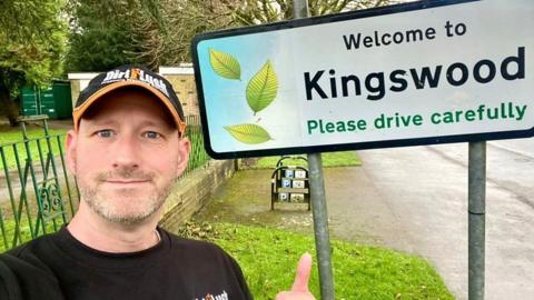 Man smiles in front of clean road sign