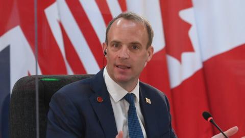 Dominic Raab delivers an address seatd before a range of flags