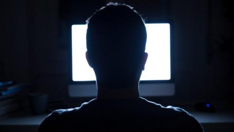 Silhouette of man's head in front of computer monitor light at night