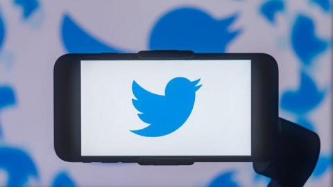 Twitter logo displayed on a smartphone in front of a Twitter logo background