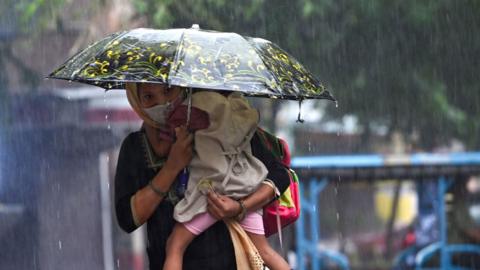 A woman carries her child beneath an umbrella amid heavy rains in New Delhi on September 15, 2023.