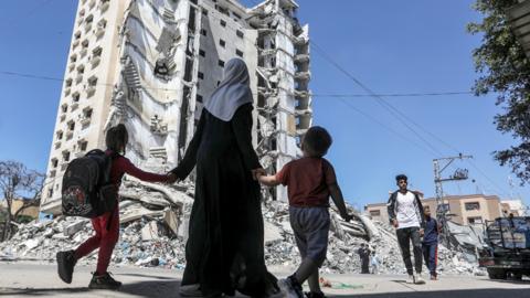 A woman and two children walking past a damaged building in Gaza
